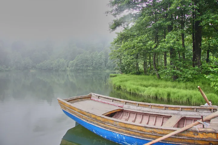 Piccola barca su un lago immerso nella nebbia, con sagome appena visibili sull'acqua ferma.