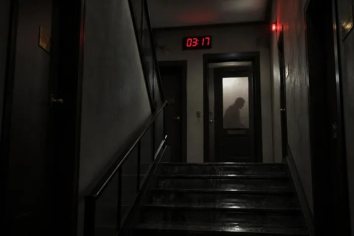 Scala condominiale buia con porte chiuse e un orologio digitale fermo alle tre e diciassette