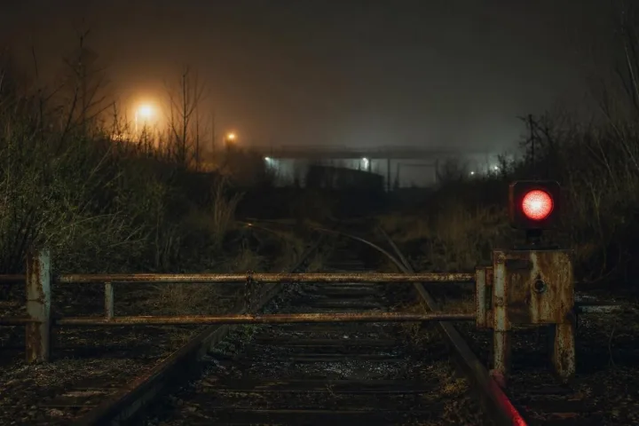 Binario ferroviario abbandonato nella nebbia con un segnale rosso acceso oltre uno scambio arrugginito
