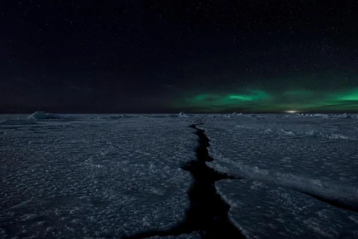 Una distesa di ghiaccio polare nella notte, attraversata da una frattura scura sotto un cielo appena illuminato
