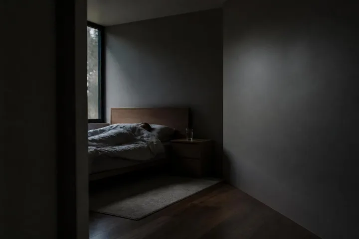 Una persona dorme in una camera buia mentre un bicchiere sul comodino vibra accanto alla parete nuda.
