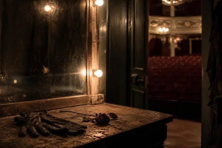 Specchio di un camerino antico con guanti neri e una rosa appassita illuminati da lampadine fioche