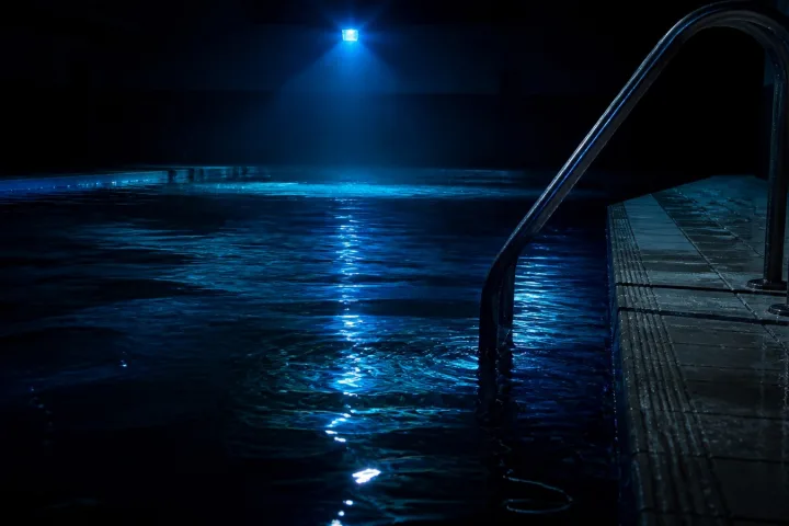Scaletta di piscina e acqua scura sotto una luce blu tremolante