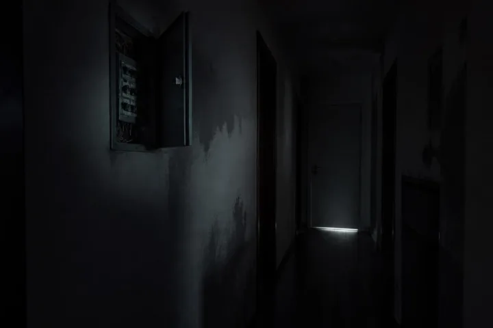 Quadro elettrico aperto in un corridoio buio con luce fredda sotto una porta chiusa