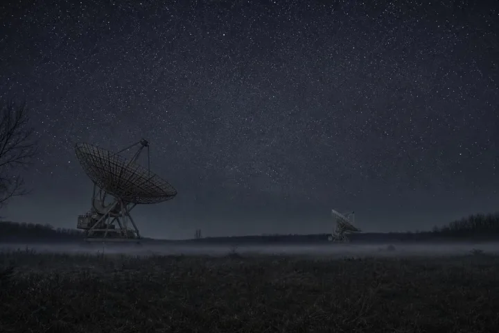 Campo notturno con radiotelescopi immersi nella nebbia sotto un cielo stellato