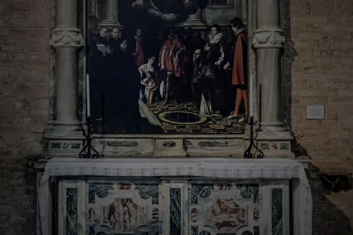 Corridoio d’abbazia in penombra con altari e luce fredda sul fondo