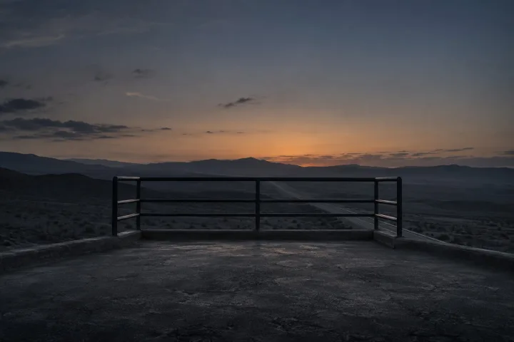 Una piattaforma di osservazione vuota lungo un'autostrada del deserto, al crepuscolo, con il cielo arancione all'orizzonte.